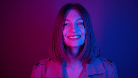 Charming Ukrainian girl looking away in neon lights. Footage of cute young woman with dazzling smile looking at camera. Editorial, studio, style, fashion.