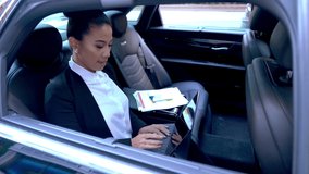 Chinese businesswoman in formal wear using digital tablet for financial marketing during transportation in executive car, attractive woman making online money transfer on touch pad