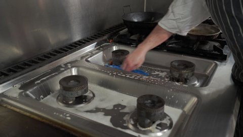Man cleaning the gas hob in a restaurant kitchen