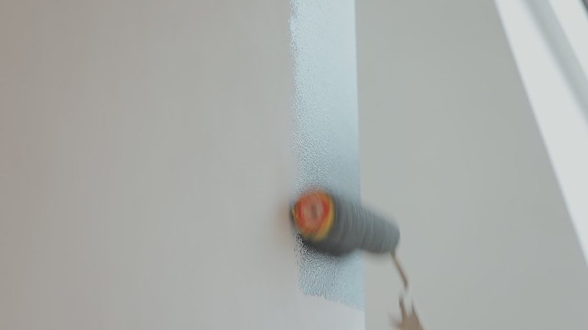 Roller painting white wall with black paint.