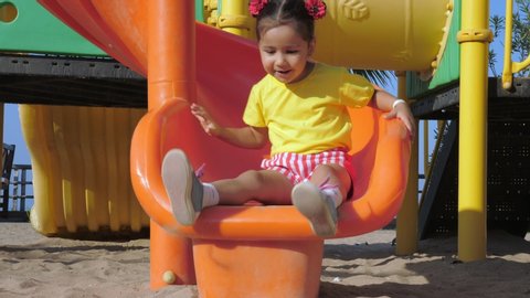 Little girl roll down a kids slide. Happy childhood concept.