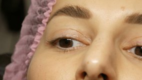 Close up face of beautiful young woman with wide hairy eyebrows and brown eyes in pink hat before the procedure for laminating eyelashes in beauty salon