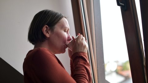 Woman drinking tea by the window in kitchen loft, looking outside and thinking