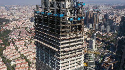 QINGDAO, CHINA – SEPTEMBER 2019: Rotating aerial view of massive construction site of skyscraper in central business district of Qingdao, with low-rise residential neighborhood in background