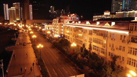 QINGDAO, CHINA – SEPTEMBER 2019: Drone flight past beautifully illuminated low-rise residential buildings, classic lampposts create romantic atmosphere in Qingdao, China