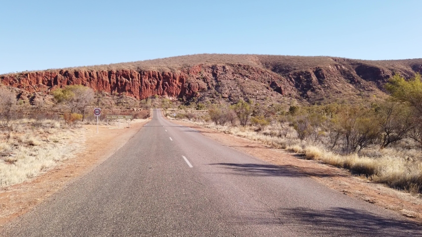 Glen Helen Gorge signboard on the road in Central Australia outback along Red Centre Way in Northern Territory. West MacDonnell Ranges on landscape background. POV running in the road.