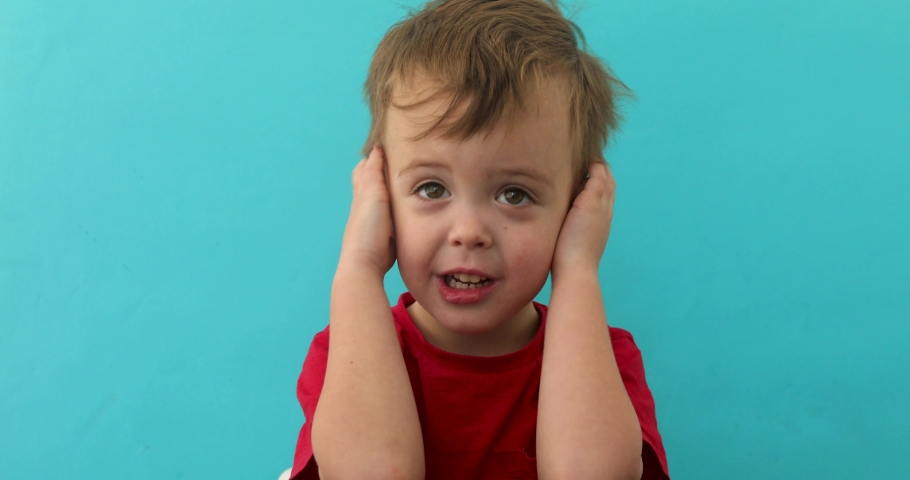 Scared boy covering ears with hands looking up on blue background Royalty-Free Stock Footage #1040989709