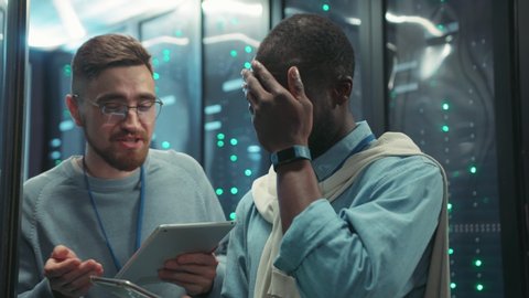 In data center head administrator arguing with young black technician critiсizing his work explaining a problem inside tech server room. Data center. Working relationships.