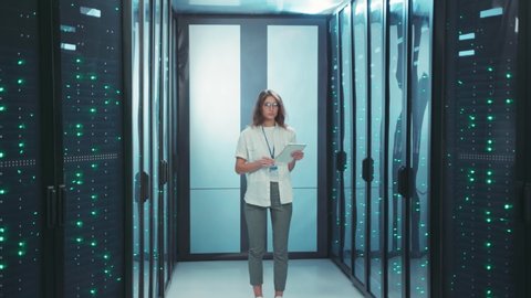 Beautiful woman IT administrator standing in technological internet server room. Female specialist working at datacentre secure storage complex.