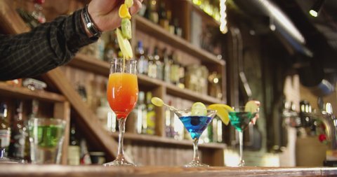 4K Professional barman decorates a cold cocktail with fruits . Bartender prepares cocktails at the beautiful bar and pours and serves a cocktail . Barman preparing colorful cocktails . Slow Motion .