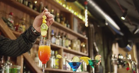 Professional barman decorates a cold cocktail with fruits . Bartender prepares cocktails at the beautiful bar and pours and serves a cocktail . Barman preparing colorful cocktails . Slow Motion .