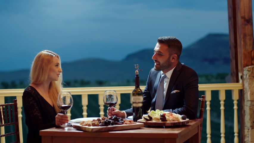 Young couple dining exclusively in a romantic atmosphere in restaurant . Pair enjoying romantic dinner in terrace near the vineyard . Couple drinking wine and making toast . Slow Motion . Royalty-Free Stock Footage #1040999516