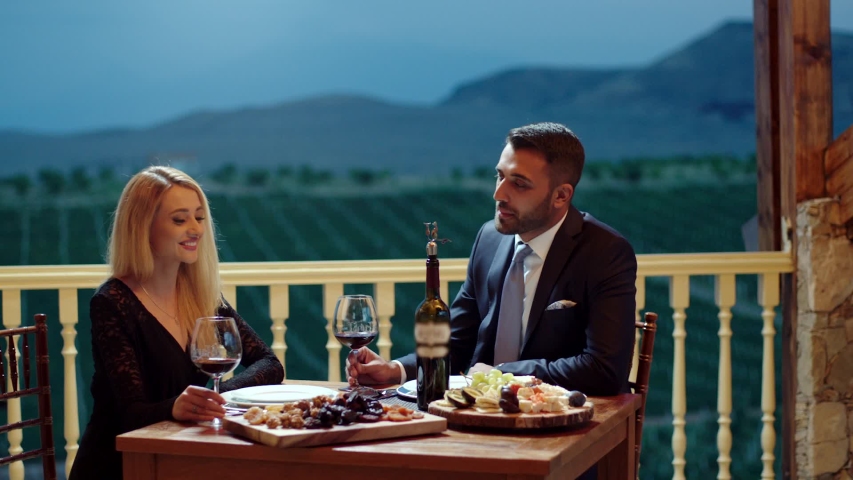 Young couple dining exclusively in a romantic atmosphere in restaurant . Pair enjoying romantic dinner in terrace near the vineyard . Couple drinking wine and making toast . Slow Motion . Royalty-Free Stock Footage #1040999519