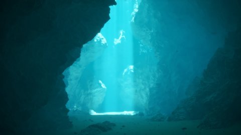 Beautiful underwater cave illuminated by sunbeams pouring through a surface opening. Moving light shafts generating caustics effects on rock formations. Travelling, deepwater scuba diving.
