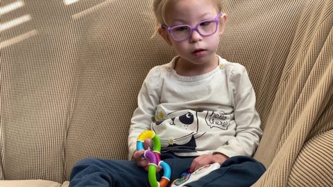 San Jose, CA - November 14, 2019: Toddler girl with lowest spectrum of autism with eye glasses rocking back and forth on a sofa at home. 
