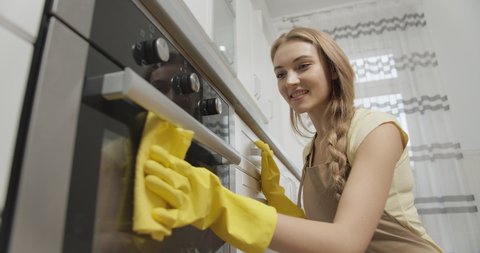 Young smiling lady with long blond hair in apron cleaning cooker, household activity