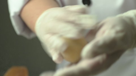 Close up of a chef hands in glove shaping rolling a round raw mooncake dough.	