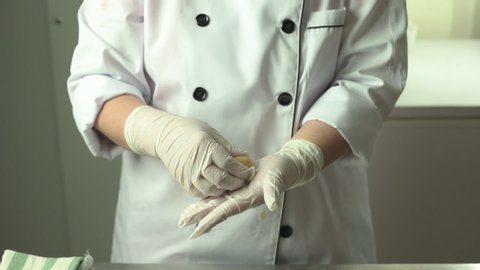 A chef in uniform with hands in glove shaping raw mooncake dough with stuffing.	