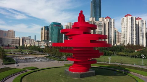 QINGDAO, CHINA – SEPTEMBER 2019: Rotating aerial view of artistic red monument on May 4 Square, located in the financial business district of Qingdao in China