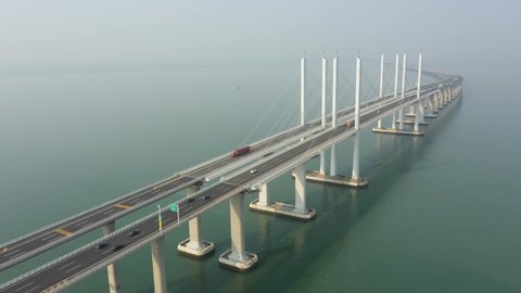Retreating aerial footage of commuting traffic (passenger vehicles and cargo trucks) driving over Jiaozou Bay Bridge, connecting the more industrial Huangdao to mostly residential Qingdao China