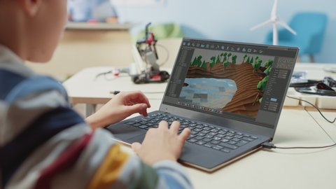 Elementary School Computer Science Classroom: Over the Shoulder View of a Kid Using Laptop to  Design 3D Game, Building Level in Strategic Roleplaying Video game