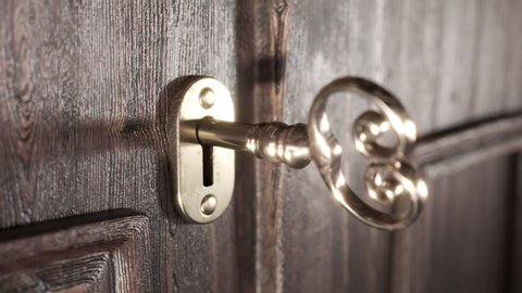 View at old-fashioned wooden doors focused on the golden lock door and door handle. Key is rotating around its pivot and opening the lock. After that, a handle is pulled and doors open. Brightness.
