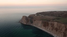 Drone flight at sunrise over the lighthouse at Cape Emine, surrounded by turquoise green sea and mountain slopes - Black sea coast, Bulgaria. 