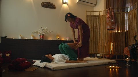 Asian Woman performs Traditional Thai Massage to beautiful European Woman. Rehabilitation and Treatment after Injuries with the help of Massage. Relax and Rest from massage of Legs, Arms and Back.