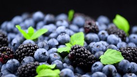 Blueberry and Blackberry background. Ripe and juicy fresh picked ripe berries rotate backdrop, closeup. Organic Blue and Black berries with a leaf rotation, macro shot. Vegan sweet food. Slow motion