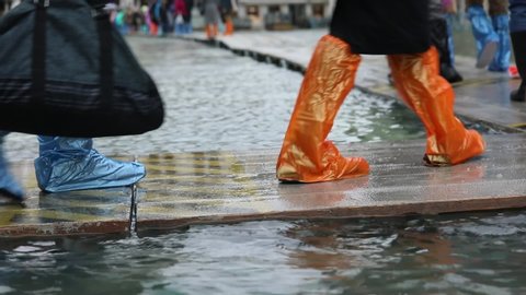 People with plastic gaiters or with boots on the walkway during the flood in Venice in Italy