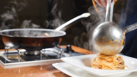 Chef serving pasta on plate. Close up. Putting pasta in plate with kitchen tongues and laddle. Italian cuisine. White steam rising in slow mo. Shot in hd