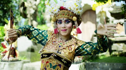 Balinese female dancer in sharp sunlight wearing ornate jewelled flowered headdress and colorful clothing with exquisite makeup Indonesia travel and tourism RED MONSTRO