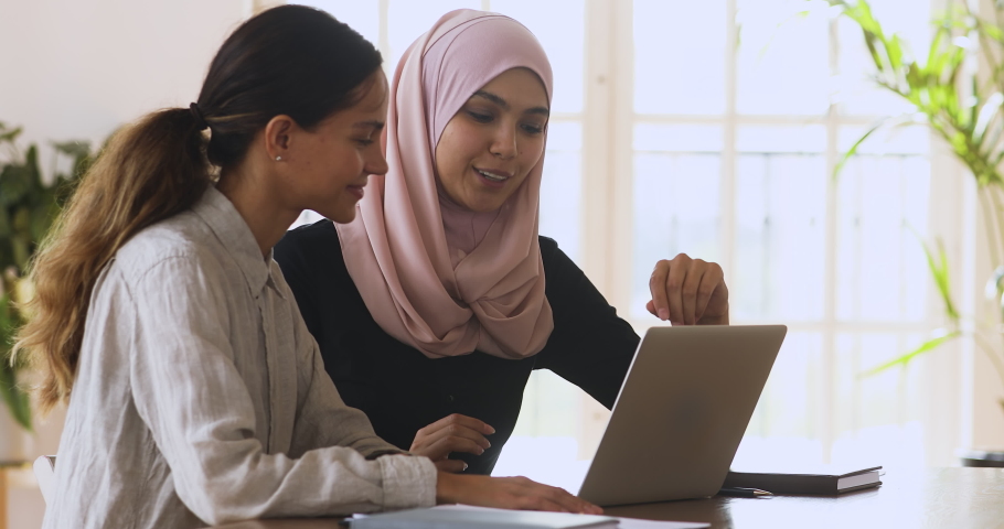 Female asian muslim manager mentor wear hijab consult caucasian client teaching intern trainee with laptop talk in office, two diverse ethnic businesswomen discuss online work at corporate meeting Royalty-Free Stock Footage #1041054044