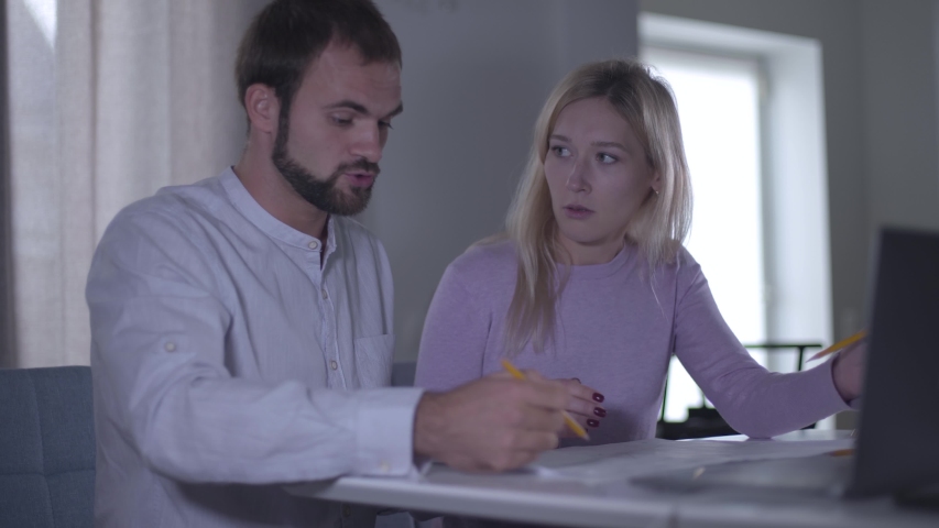 Tired Caucasian woman discussing the project with her male colleague. Bearded man explaining his vision to the cute coworker. Professional architects working on drawings for interior design. | Shutterstock HD Video #1041057734