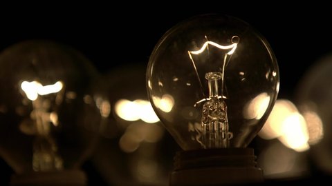 The incandescent lamp with a tungsten filament wobbles on the wire. The light flashes . Light from a light bulb. Bulb close-up.