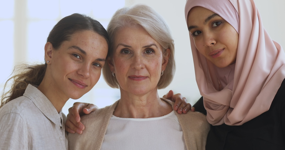Three diverse smiling young and old women friends colleagues embracing looking at camera, happy beautiful different generations asian muslim and caucasian ladies bonding together, close up portrait Royalty-Free Stock Footage #1041062039