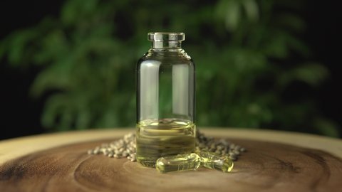 Extreme close up of the glass jar bottle with medical cannabis cbd oil concentrated resin dosing and diluted with a carrier oil for oral administration. On wood table and green hemp plant background.