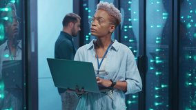 Black female IT engineer upgrading hardware in rack server room corridor working on computer laptop cooperating with male specialist at big data center. - Powered by Shutterstock - Get 15% off with code: PIKWIZARD15