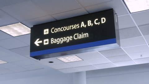 Sign at an airport directing travelers to concourses and baggage claim. Signboard on the ceiling directs commuters to where they need to go. Interior of an airline terminal shows flying and tourism.
