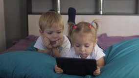 happy family a concept little children play digital tablet. young kids watch videos on a white digital tablet. brother lifestyle and sister are resting lie on the bed holding tablet online chat