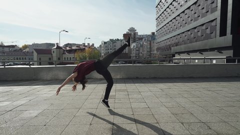 Young female gymnast runs in the city and doing a series of flips on training area near modern buildings.