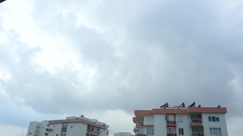Dark grey thunderstorm clouds running fast over roofs of houses in city. Real time full hd video footage.
