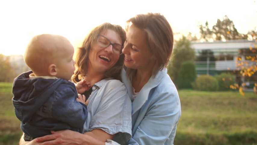 Two young girls and one year old baby, close portrait. Samesex couple with a child for a walk in the autumn park. The kid pushes the second woman. Royalty-Free Stock Footage #1041086194