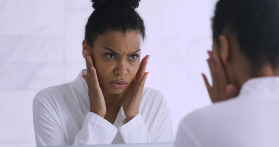 Worried african american lady upset with dry fragile skin looking in mirror, unhappy stressed mixed race woman checking wrinkles troubled with acnes touching face having facial skin problem concept | Shutterstock HD Video #1041087334