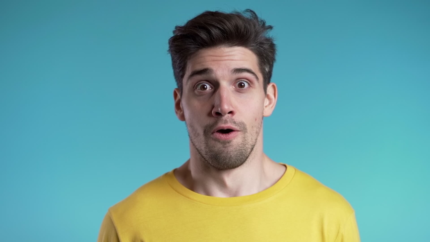 Amazed european man shocked, saying WOW. Handsome guy with stylish hairdo surprised to camera over blue background. Royalty-Free Stock Footage #1041091162