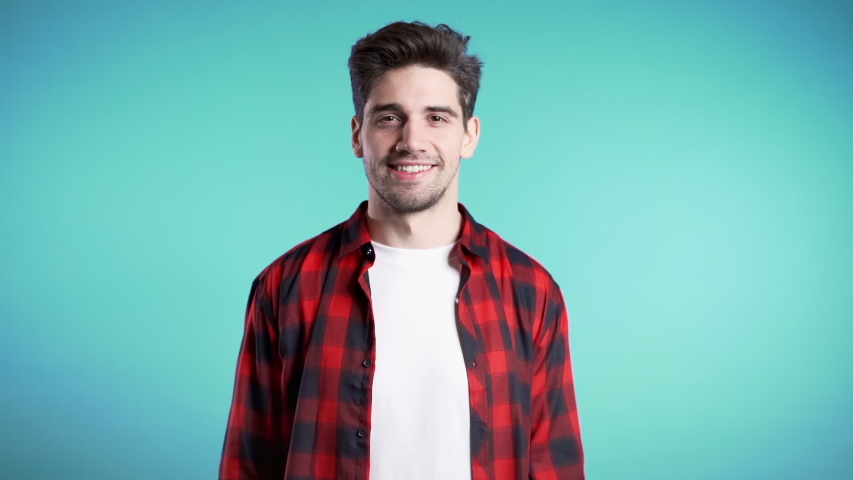 Positive young man smiles to camera. Hipster guy showing thumb up sign over blue background. Winner. Success. Body language. Royalty-Free Stock Footage #1041091171