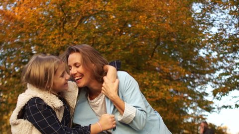 Happy family, young mother and teenage daughter have fun cuddling in the autumn park at sunset. Mothers Day
