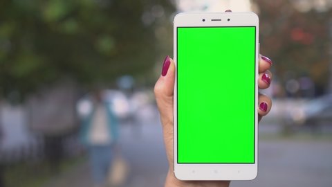 Close up hands woman holding use white phone with green screen on busy street background scrolling pages swiping surfing internet technology.smartphone chroma key message