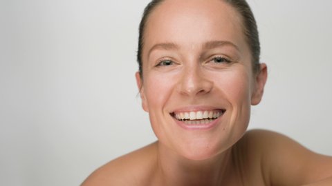 Close-up beauty portrait of young woman with smooth healthy skin, she gently touches her face with her fingers on white background and smiles
