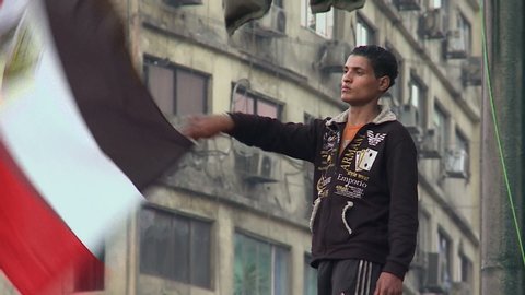 CAIRO, EGYPT - DEC 2011: Young man waves Egyptian flag during protesters against military rule at Tahrir Square while demanding parliamentary elections